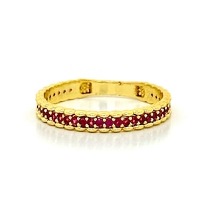 May include: A gold band ring with a row of red ruby stones.
