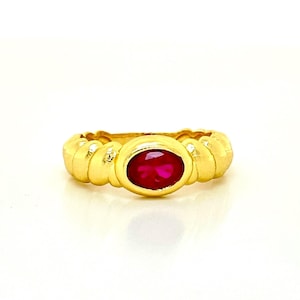 May include: A gold ring featuring a red oval gemstone set in the centre. The band of the ring is twisted and has a textured design.