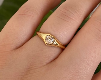 Könnte beinhalten: Ein goldener Ring mit einem herzförmigen Edelstein. Der Ring hat ein glattes, poliertes Band und eine Lünettenfassung, die den herzförmigen Stein hält. Der Ring wird an einem Finger getragen.