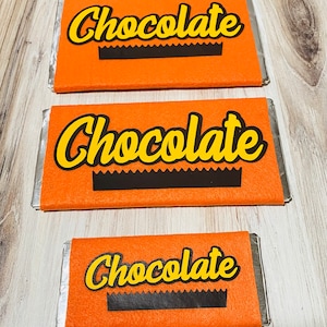 May include: Three orange felt chocolate bar wrappers with the word "Chocolate" printed in yellow letters. The wrappers are different sizes.