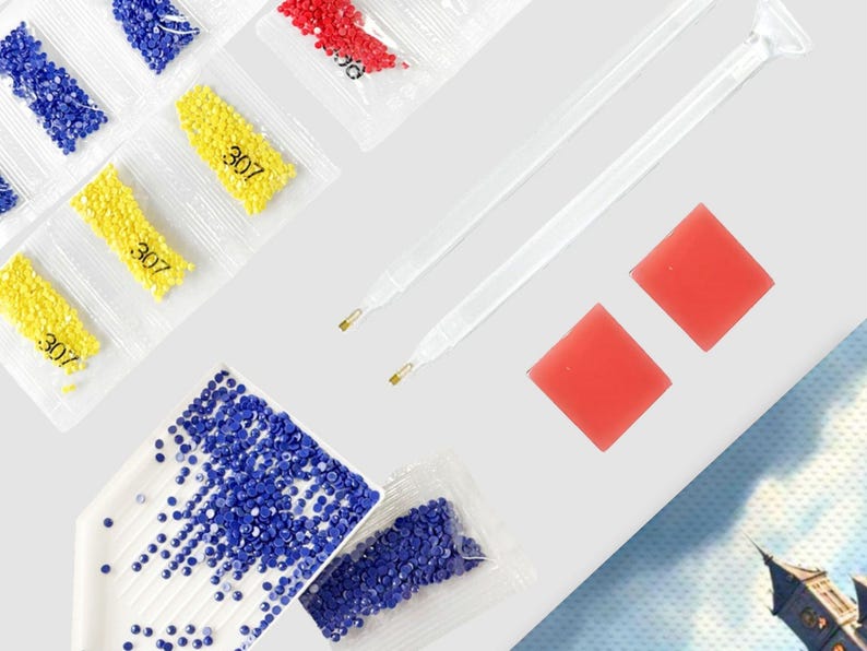 May include: An assortment of diamond painting supplies, including packets of blue, red, and yellow diamond beads, labeled with the number "307". Also included are two clear applicator pens and two square red wax pads, all arranged on a white surface.