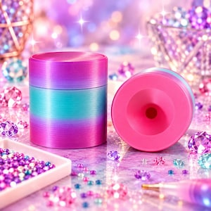 May include: A cylindrical metal container featuring a vibrant gradient of pink, purple, and teal colors. The container has a smooth, brushed texture and a circular opening on the top surface. It is surrounded by scattered colorful rhinestones.