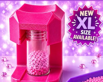 May include: A bright pink diamond painting funnel stand holding a clear glass jar filled with small pink beads. The text reads DIAMOND PAINTING FUNNEL and NEW XL SIZE AVAILABLE. Several loose pink beads are scattered around the base.