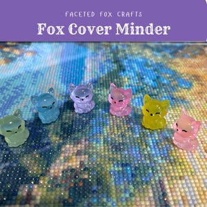 May include: A selection of translucent fox-shaped cover minders in various colours, including green, blue, purple, pink, and yellow. The text "Faceted Fox Crafts" and "Fox Cover Minder" are displayed above the minders.
