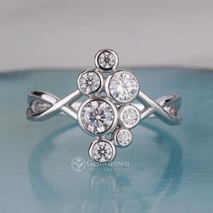 Puede incluir: Un anillo de plata con un grupo de piedras preciosas redondas y transparentes engastadas en una banda delicada e entrelazada.