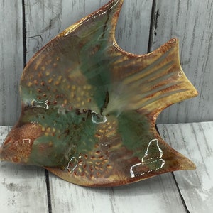 May include: A ceramic bird-shaped dish with a green, brown, and yellow glaze. The dish has a speckled texture and white accents.