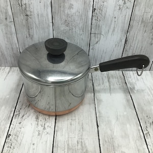May include: A silver saucepan with a copper bottom and a black handle. The saucepan has a lid with a black knob.