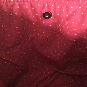 Pu&ograve; includere: Tessuto rosso con un motivo a pois di vari colori. Il tessuto ha un piccolo bottone rotondo di metallo al centro.