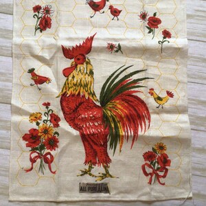 May include: A white tea towel with a red rooster and yellow chicks, red poppies, and a yellow honeycomb pattern. The text "Guaranteed All Pure Linen" is printed at the bottom.