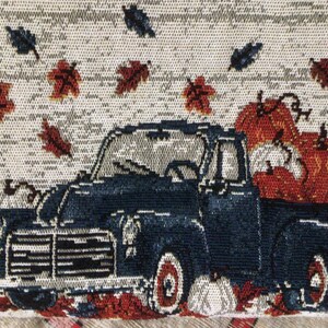 Pu&ograve; includere: Un camioncino vintage blu con una cassone pieno di zucche arancioni. Il camioncino sta guidando attraverso un campo di foglie autunnali che cadono.