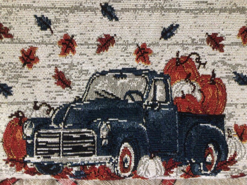 Pu&ograve; includere: Un camioncino vintage blu con una cassone pieno di zucche arancioni. Il camioncino sta guidando attraverso un campo di foglie autunnali che cadono.