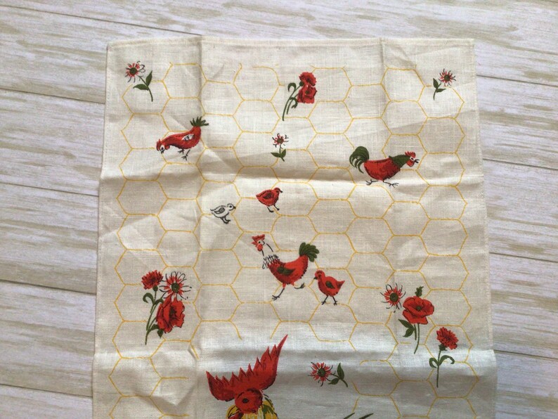 May include: A white tea towel with a yellow honeycomb pattern and red and white chickens and flowers.
