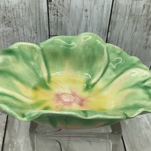 May include: A green and yellow ceramic bowl shaped like a flower. The bowl has a pink center with a white dot in the middle.