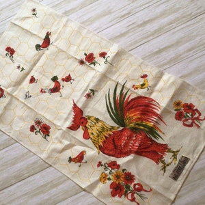 May include: A white tea towel with a red rooster and yellow flowers on a honeycomb pattern. The text "All Purpose Linen" is printed in the bottom right corner.