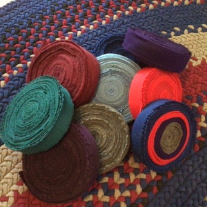 May include: Assortment of fabric scraps rolled into circles, in various colors including teal, red, purple, brown, and blue. The fabric scraps are arranged on a woven rug with a pattern of red, blue, and beige.