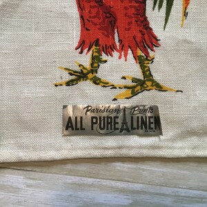 May include: A white linen tea towel with a rooster design and a silver label that reads "Parisian Prints All Pure Linen".