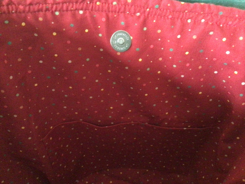Pu&ograve; includere: L'interno di una borsa tote rossa con una piccola tasca e un motivo a pois bianchi. La borsa ha una chiusura a scatto in metallo argentato.