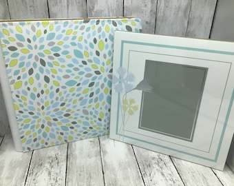 May include: Two photo albums with a white background. The album on the left has a blue, green, and yellow pattern. The album on the right has a blue border and a floral design.