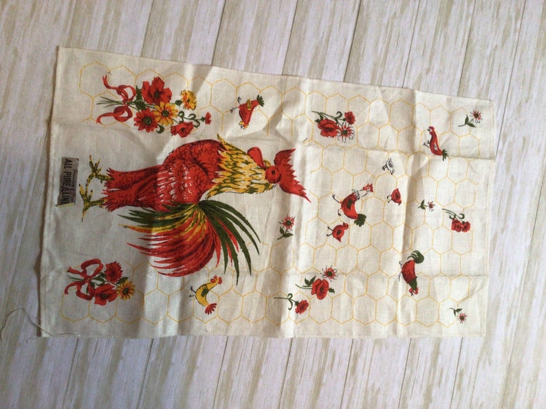 May include: A vintage kitchen towel with a red rooster and yellow chicks on a white background with a honeycomb pattern. The towel has red flowers and green leaves. The text "All Pure Linen" is printed on the towel.