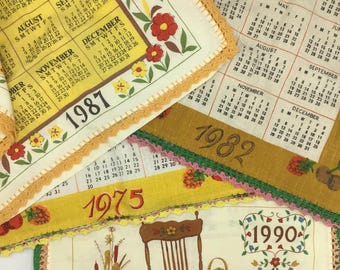 May include: Four vintage calendars with crocheted trim. The calendars are yellow and feature floral designs. The years on the calendars are 1975, 1982, 1987, and 1990.