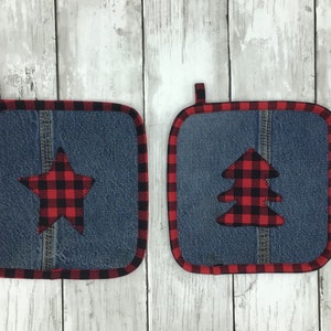 May include: Two denim pot holders with red and black buffalo plaid fabric accents. One pot holder features a star and the other features a Christmas tree.
