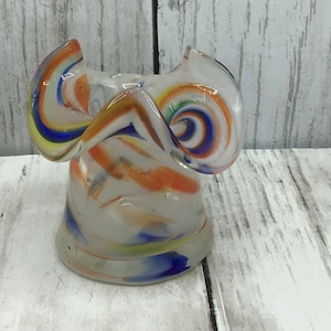 May include: A small, clear glass vase with a swirled pattern of orange, blue, and yellow. The vase has a ruffled top and a rounded bottom.