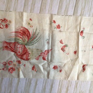 May include: A vintage linen tea towel with a red rooster and floral design. The rooster is facing right and has a green tail. The flowers are red and white.