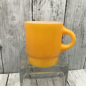 May include: A yellow ceramic mug with a rounded handle. The mug is sitting on a clear glass surface.