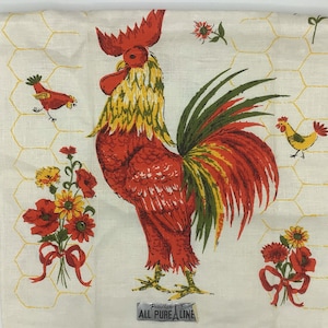 May include: A red, yellow, and green rooster with a long tail is printed on a white linen tea towel with a yellow honeycomb pattern. The text "Pure Linen" is printed on a label at the bottom of the towel.