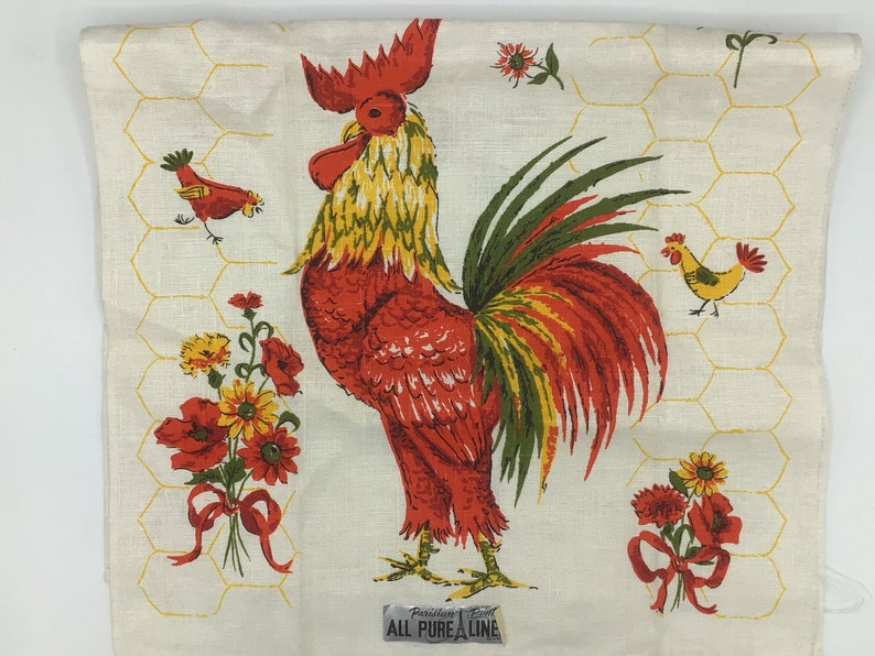 May include: A red, yellow, and green rooster with a long tail is printed on a white linen tea towel with a yellow honeycomb pattern. The text "Pure Linen" is printed on a label at the bottom of the towel.