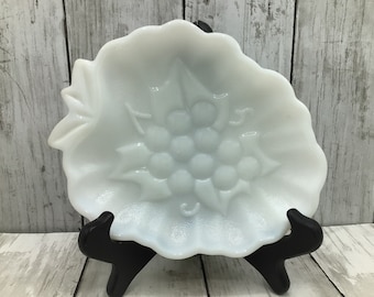 May include: White milk glass dish with a grape design. The dish is shaped like a leaf and has a scalloped edge.