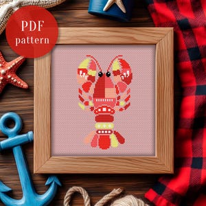 May include: A framed cross-stitch pattern featuring a colorful lobster design. The lobster is primarily red with yellow and pink accents, set against a pink background. The frame is made of light-colored wood. The text "PDF pattern" is in a red circle in the upper left corner.