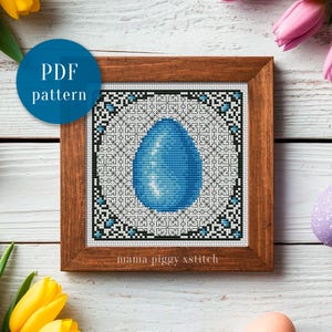 May include: A framed cross-stitch pattern featuring a blue egg design. The egg is centered within a geometric border of black, white, and blue. The words "PDF pattern" are in a blue circle in the upper left corner. The frame is made of wood.