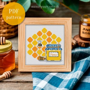 Peut inclure: Un motif de point de croix encadré représentant un nid d'abeilles, une abeille et un pot de miel. Le pot est étiqueté "Honey". Le cadre est en bois clair. Le texte "PDF pattern" est dans un cercle jaune en haut à gauche.