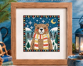 May include: A framed cross stitch pattern featuring a brown bear wearing a striped scarf against a snowy mountain landscape with a crescent moon and stars. The text "PDF cross stitch pattern" and "mama piggy xstitch" appear on the image.