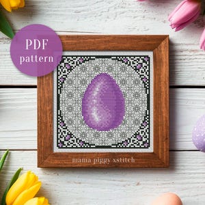 May include: A framed cross-stitch pattern showing a large purple Easter egg. The egg is surrounded by a geometric border in black, white, and purple. The text "PDF pattern" is in a purple circle. The frame is made of wood.