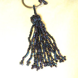 May include: A black beaded necklace with a tassel. The necklace has a silver ring clasp and the tassel is made of iridescent black beads.