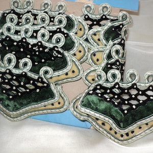 May include: A set of green and black velvet appliques with a white and green embroidered trim. The appliques are shaped like a rectangle with rounded corners and have a decorative design.