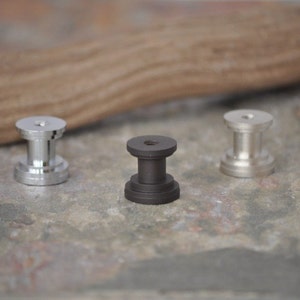 Peut inclure: Trois boutons en m&eacute;tal dans diff&eacute;rentes finitions&nbsp;: argent, noir et nickel. Les boutons sont ronds avec un centre sur&eacute;lev&eacute; et un trou filet&eacute; au bas.
