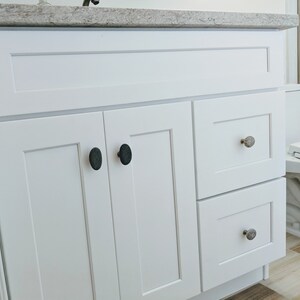 Peut inclure: Vasque de salle de bain blanc avec deux portes de placard et deux tiroirs. Les portes des placards ont des boutons ovales noirs et les tiroirs ont des boutons ovales argent&eacute;s.