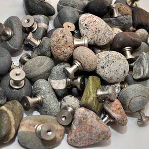 Peut inclure: Une collection de tirettes de tiroir en pierre naturelle lisse avec des ferrures en m&eacute;tal argent&eacute;. Les pierres sont de diff&eacute;rentes nuances de gris, brun et vert.