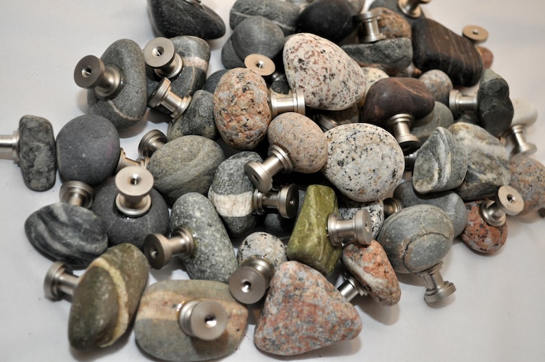 Peut inclure: Une collection de tirettes de tiroir en pierre naturelle lisse avec des ferrures en m&eacute;tal argent&eacute;. Les pierres sont de diff&eacute;rentes nuances de gris, brun et vert.