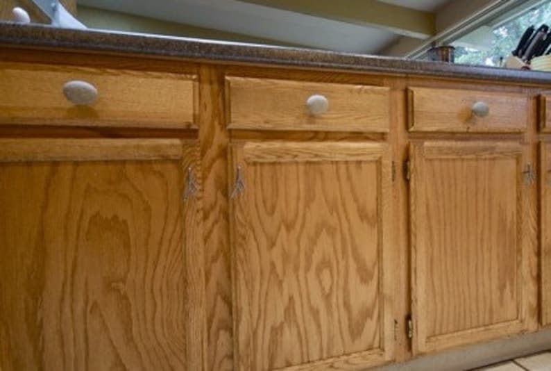 Peut inclure: Gros plan sur un ensemble d'armoires de cuisine en bois avec une finition en bois clair. Les armoires ont des boutons ronds simples et sont dispos&eacute;es en rang&eacute;e.
