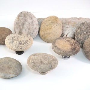 May include: A set of eight smooth, round, natural stone drawer pulls in various shades of brown and gray. The pulls are attached to metal bases.