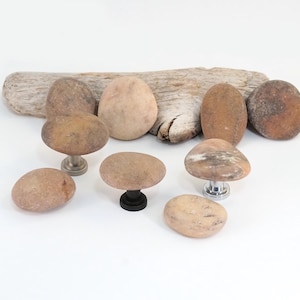 May include: A set of eight smooth, natural stone cabinet knobs in various shades of brown and beige. The knobs are attached to metal bases.