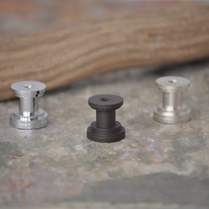 May include: Three metal knobs, one silver, one black, and one silver. The knobs are round with a raised center and a threaded hole on the bottom.