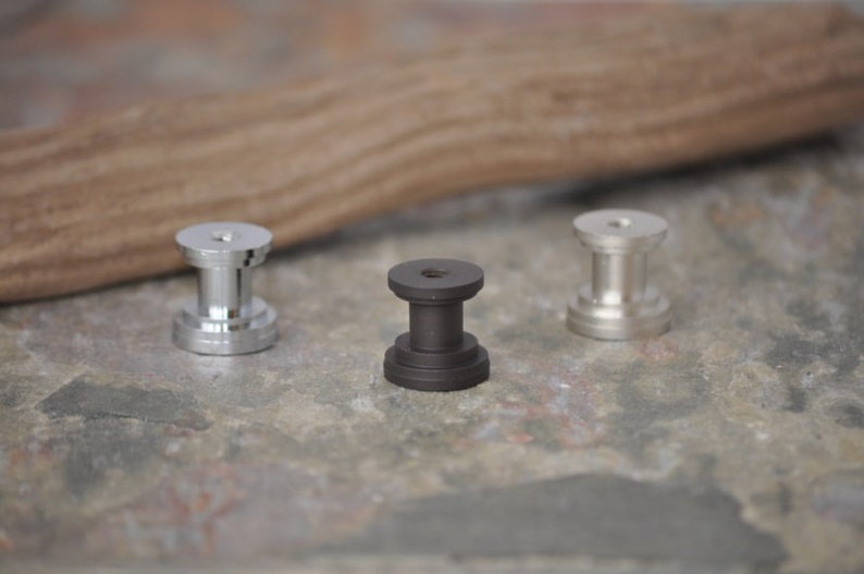 May include: Three metal knobs, one silver, one black, and one silver. The knobs are round with a raised center and a threaded hole on the bottom.