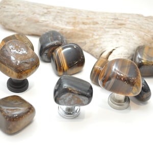 May include: A set of eight tiger's eye stone cabinet knobs. The knobs are in various shapes and sizes, with a natural, polished finish. The knobs are mounted on silver and black metal bases.