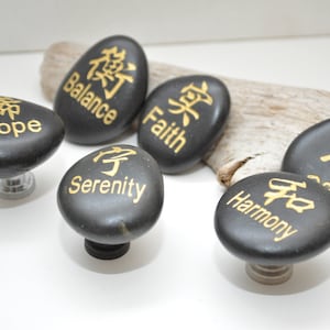 May include: Six black smooth stones with gold lettering. Each stone has a different word and Chinese character: Hope, Balance, Faith, Serenity, Harmony, and Peace.