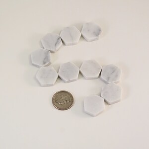 May include: A set of white marble hexagon tiles arranged in a curved pattern. A US quarter is included for scale.